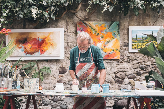 Man painting pottery in front of brick wall.